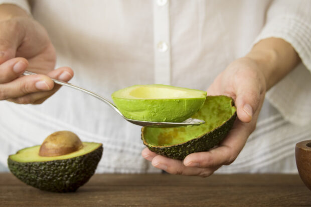 Donna che scava la polpa di un avocado con un cucchiaio