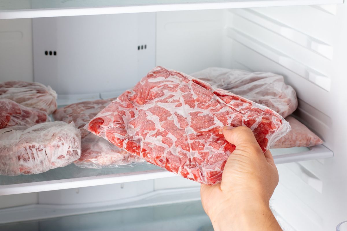 Uomo che prende in mano della carne congelata dal congelatore del frigorifero
