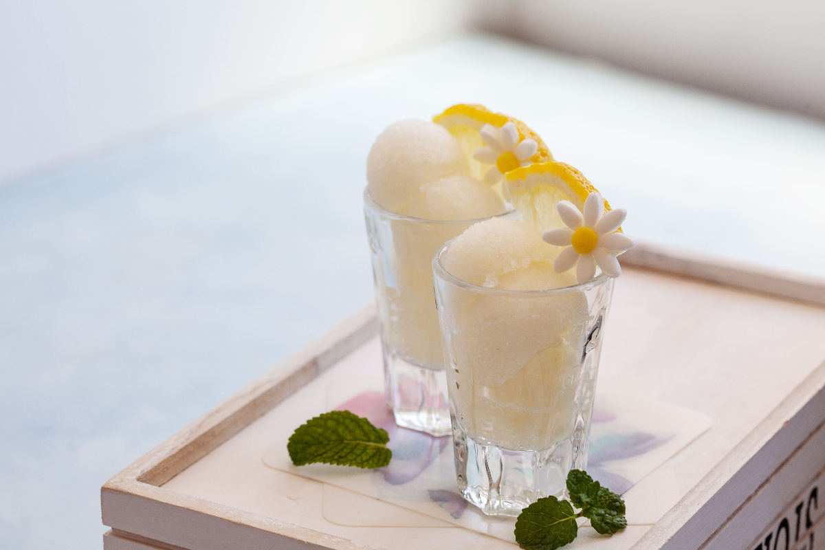 Coppia di sorbetti al limone su un tavolino di legno, con sfondo bianco, guarniti da una fetta di limone e da foglie di menta