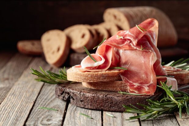 Prosciutto di Carpegna tagliato assieme a del pane su sfondo di legno