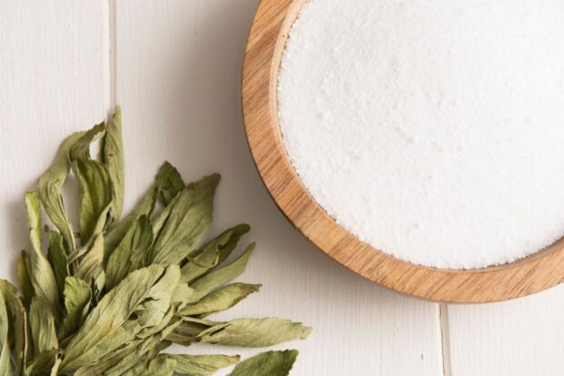 Stevia, dolcificante naturale, in foglie e in forma granulare (in ciotola) su sfondo bianco.